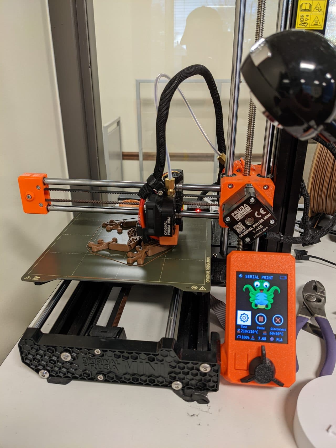 Close-up of the Original Prusa MINI+ at OCPL showing the printer frame, filament spool, and the LCD control interface.